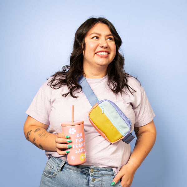 Blue background with a girl smiling wearing a small peri mint block color with a blue strap hip bag, holding a pink "oh for fucks sake" cold cup 