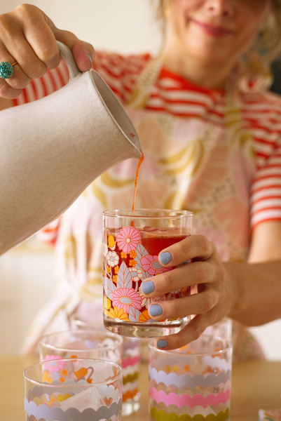 Girl pouring a drink inside of a rocks glass cup with flowers on it.