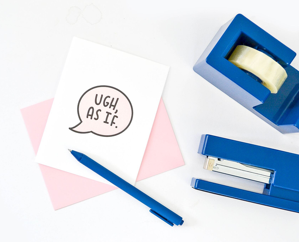 White greeting card with a text bubble in black and light pink with "Ugh, As If." There is a pink envelope, a blue jotter pen, blue tape dispenser and blue stapler next to it. 