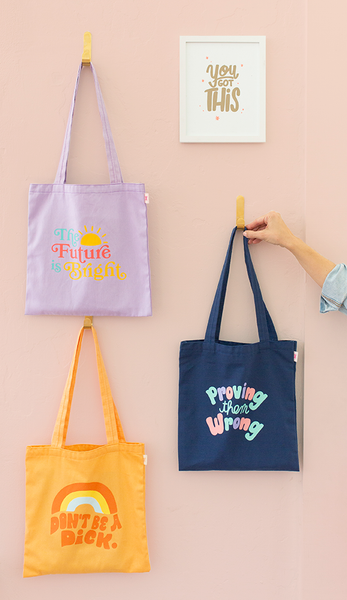 three canvas tote bags with fun sayings on them hung on a wall 