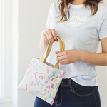 Smiling girl holding a cute tiny bag in rainbow confetti print.