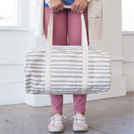 Girl in white sneakers holding a gray and white striped canvas duffel bag.