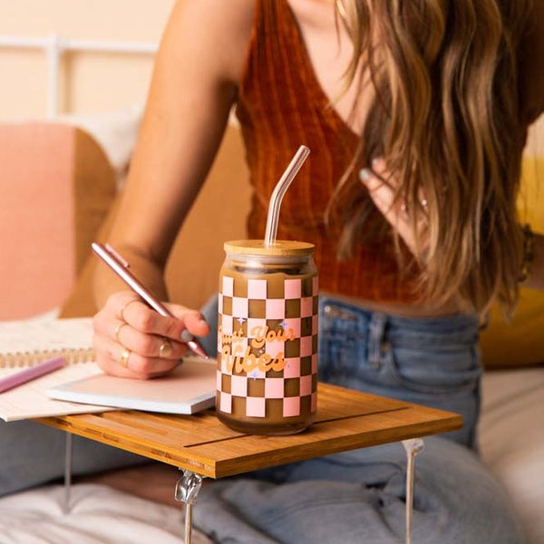 Woman using the "Trust Your Vibes" can glass w/lid + straw while writing with a TOOT pen in an extra-small notepad. 