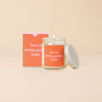 A 8 oz. candle jar with lid, with an orange decal on it "You're doing great, babe" printed on.