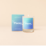 Candle rocks glass with light-to-dark blue ombre decal and text that reads "Pisces" with minimalist, white sparkle stars surrounding the text; "the dreamer at heart" sits at the bottom of the decal. Box packaging with the same design sits behind glass.