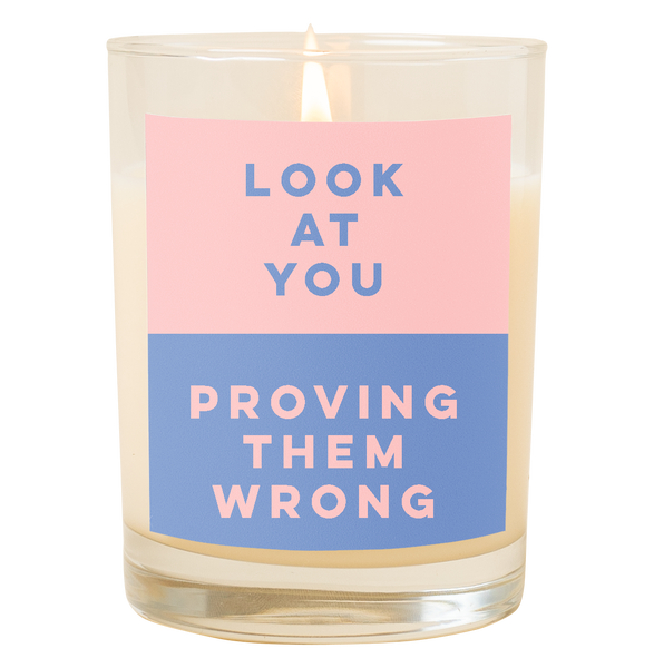 A candle with a decal that says, "Look at you, proving them wrong." Top half is a pastel pink color and bottom half of decal is a dusty blue color.