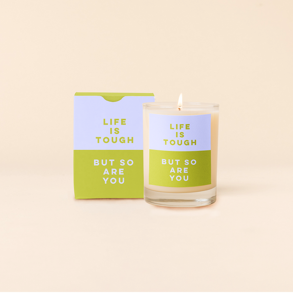 Rocks candle with two tone backdrop. Top half blue backing with green text and bottom half green backing with blue text reading "LIFE IS TOUGH BUT SO ARE YOU". Two tone box packing with same text as candle.
