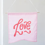 Hand holding a cute wall hanging in pink canvas with the word love.