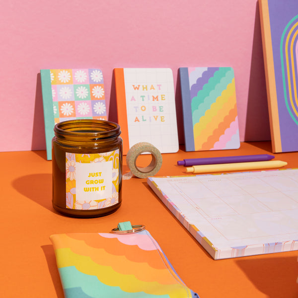 "Just Grow With It" candle with other of Elizabeth Olwen's collection items which include notebooks, a pouch, planner pad, and jotter pens.
