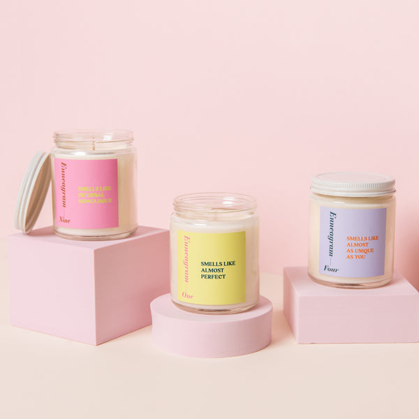 Three Enneagram candles with lids displayed in front of pink background.