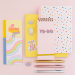 stack of different sized notebooks with different patterns, metallic pens and enamel pins