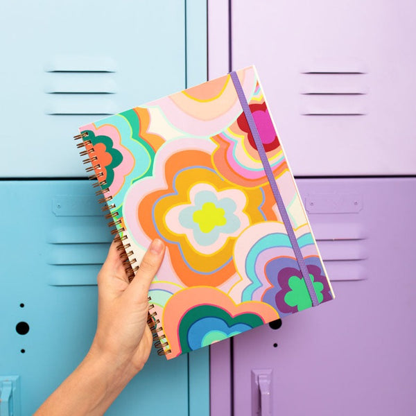 a hand holding a small goal getter planner with multicolor flowers all around the binder and a purple elastic band to keep it closed.