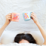 girl in bed with covers over her head holding two coffee mugs with sassy sayings