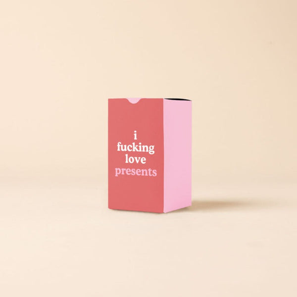 A candle box with three pink sides and a red side with the phrase "i fucking love presents" on it.