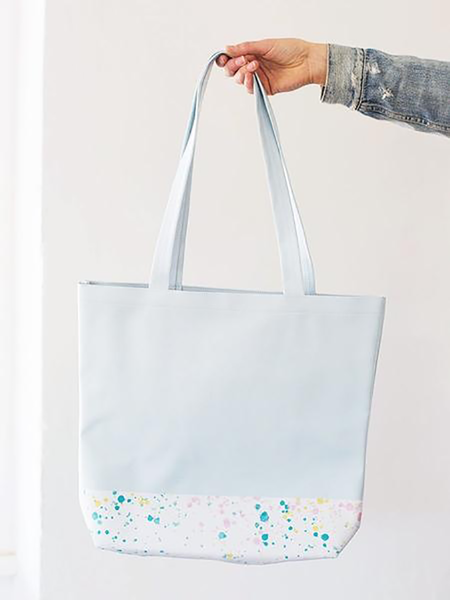 Girls hand holding a cute tote bag in powder blue with a white paint splatter detail along the bottom.