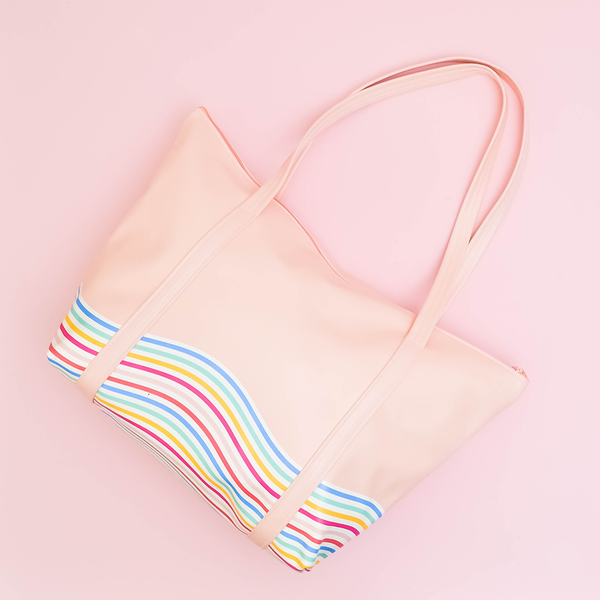 Weekender bag is laid on a pink surface, with it's straps raised above the zipper and the rainbow patters clearly visible. 