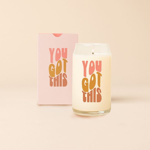 Can glass candle with text that says "YOU GOT THIS" in wavy, multi color font. Box packaging with same design sits behind candle.