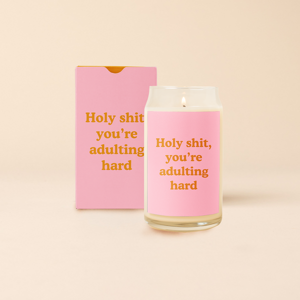 16 oz candle can glass with pink decal and text that reads "Holy shit, you're adulting hard" in red font. Pink box with same design sits behind candle.