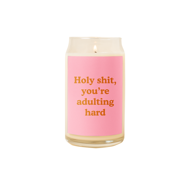 A 16 oz. candle with a pink decal that says "HOLY SHIT YOU'RE ADULTING HARD."