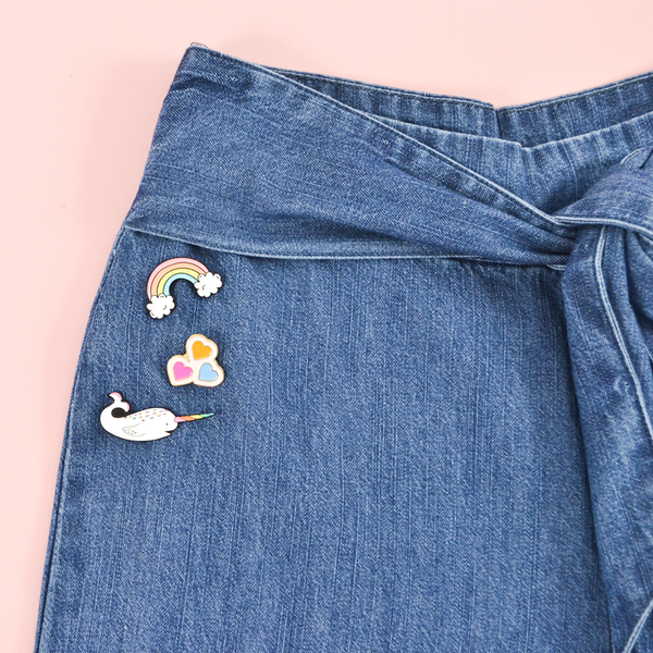 Our rainbow, hearts, and narwhal enamel pins pinned to a denim pair of jeans.