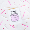 A white greeting card with a pink, black and white birthday cake. On top of the cake is a banner with the text 