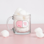 Lifestyle photo of a chill pill glass mug filled with cotton balls on a pink table.