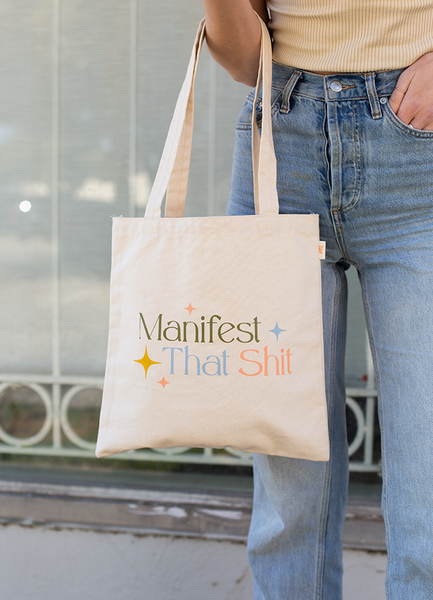 Person holding a Natural canvas Main Squeeze tote with Manifest That Shit logo.