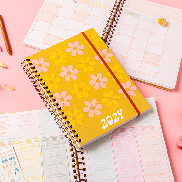 Day to Daisy 2024 Dated Goal Getter Planner laying on an open planner with jotter pens and "here comes the sun" enamel pin