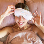 Woman wearing a Multi-Colored Sleep masked with band that reads Manifest That Shit. Includes an abstract squiggle pattern on the trim and head band support.