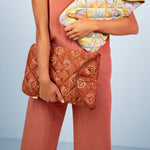 Light blue background with a girl holding a puffy brown, colorful smiley faces all over laptop sleeve on one hand and the kaleidoscope pattern laptop sleeve on the other   