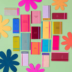 Image contains multiple notebooks, taskpads, and notepads against a light green backdrop and different colored flower props. Large notebooks dimensions are 4.5" W x 8.125" H and mini notebooks dimensions are 4.5" W x 6" H, both with tape binding, and elastic closure. Taskpads dimensions are 3" W x 7" H with coil binding and elastic band closure. Tearaway notepads with gluetop binding and dimensions  3.5" W x 7" H. 