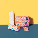 A collage of a Betty Bloom Jitterbug, Betty Bloom Puffy Busier Bee, Betty Bloom Taskpad and Betty Bloom desk calendar. The Betty Bloom pattern features an all over colorful daisy pattern on top of a light pink background. There is also an orange Jotter resting on top of the taskpad.