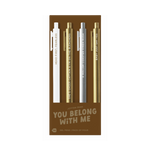A pack of four gel jotter pens displayed on bronze packaging labeled “YOU BELONG WITH ME.” Each pen features a metallic or neutral tone with Taylor Swift-inspired lyrics:
