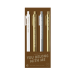 A pack of four gel jotter pens displayed on bronze packaging labeled “YOU BELONG WITH ME.” Each pen features a metallic or neutral tone with Taylor Swift-inspired lyrics:

White pen: “HEAD FIRST, FEARLESS”

Gold pen: “SHE’S CHEER CAPTAIN & I’M ON THE BLEACHERS”

Silver pen: “A ROLLER COASTER KINDA RUSH”

Gold pen: “BABY JUST SAY YES”