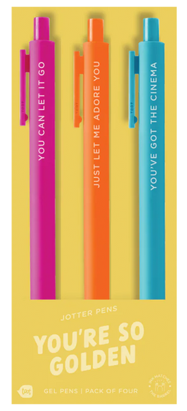 A set of three colorful jotter pens on yellow packaging labeled “YOU’RE SO GOLDEN.” The pink pen says “YOU CAN LET IT GO,” the orange pen reads “JUST LET ME ADORE YOU,” and the blue pen says “YOU’VE GOT THE CINEMA.” The packaging notes this is a pack of four gel pens, though one pen is not shown.