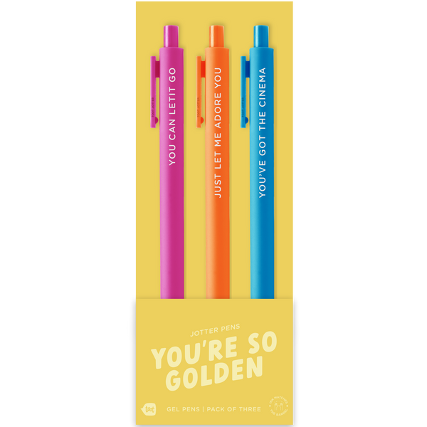 A set of three colorful jotter pens on yellow packaging labeled “YOU’RE SO GOLDEN.” The pink pen says “YOU CAN LET IT GO,” the orange pen reads “JUST LET ME ADORE YOU,” and the blue pen says “YOU’VE GOT THE CINEMA.” The packaging notes this is a pack of four gel pens, though one pen is not shown.