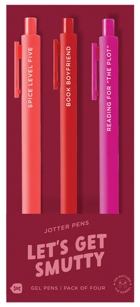 A set of three bold-colored jotter pens on deep red packaging labeled “LET’S GET SMUTTY.” The coral pen says “SPICE LEVEL: FIVE,” the red pen reads “BOOK BOYFRIEND,” and the magenta pen says “READING FOR ‘THE PLOT’.” Packaging notes it’s a gel pen pack of four, although only three pens are visible, and ink matches the barrel color.
