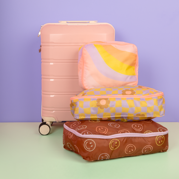 Purple background and a pink suitcase with a cool funky daisy cube set on a pastel green surface.