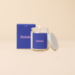 A Yippie Toot Candle Jar with Lid that says Delulu in pink on a royal blue like background with a matching box. 