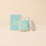 A Yippie Toot Candle Jar with Lid that says Dumb bitch in citron on a turquoise background with a matching box. 