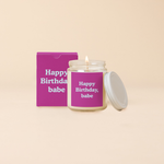 A Yippie Toot Candle Jar with Lid that says Happy Birthday Babe in blue on a purple background with a matching box 
