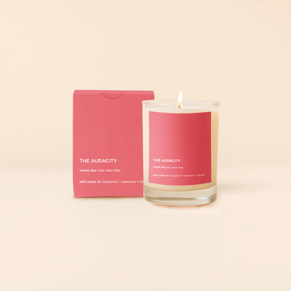 A lit 14oz rocks glass candle with the words "The Audacity" written in pink ". There is a matching box in the pink color with the same saying on it. The candle is all natural soy-based wax (paraffin-free)!! 