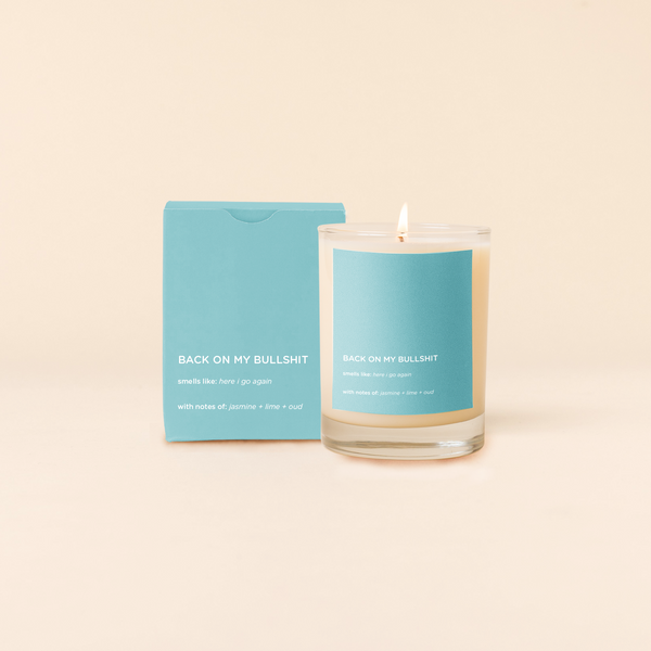 A lit 14oz rocks glass candle with the saying "Back On My Bullshit" written on a light blue sticker. There is a matching box in the light blue color with the same saying on it. The candle is all natural soy-based wax (paraffin-free)!! 
