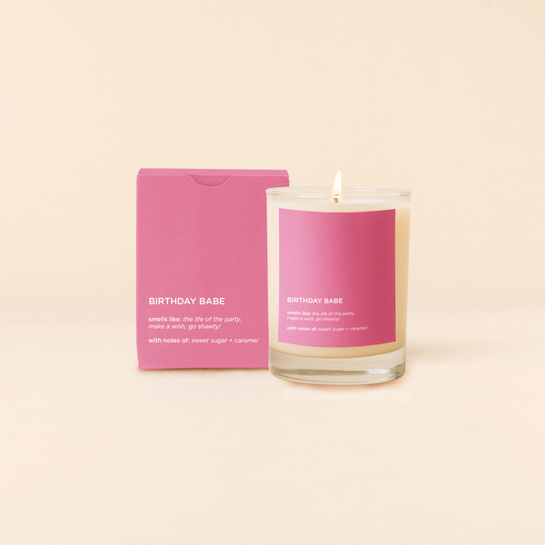A lit 14oz rocks glass candle with the words "Birthday Babe" written on a pink sticker. There is a matching box in the pink color with the same saying on it. The candle is all natural soy-based wax (paraffin-free)!! 