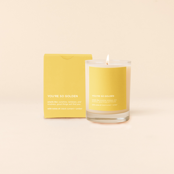 A lit 14oz rocks glass candle with the saying "You're So Golden" written on a golden yellow sticker. There is a matching box in the golden yellow color with the same saying on it. The candle is all natural soy-based wax (paraffin-free)!! 