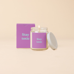 A Yippie Toot Candle Jar with Lid that says Stay Toxic in turquoise on a purple background with a matching box. 