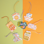 Seven different Talking Out Of Turn air fresheners laid out on a green and orange background. 