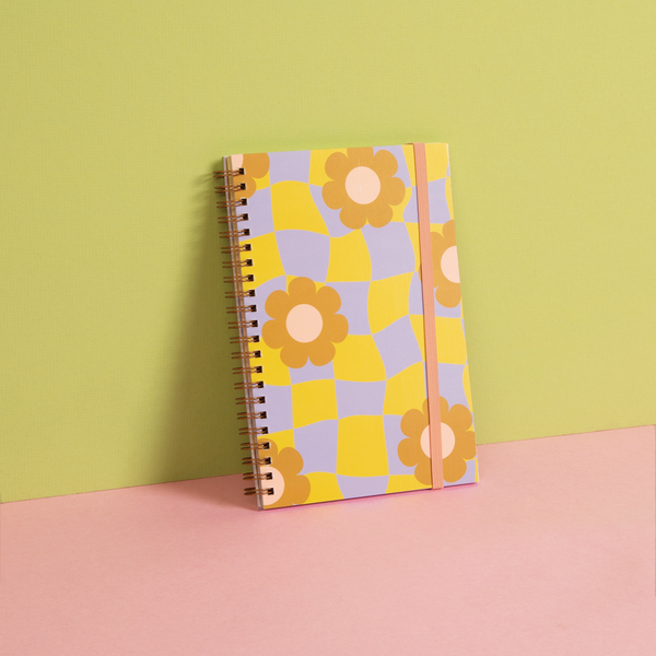 Pastel green with a pastel purple and green checkers with flowers pattern notebook with a pink strap on a pink surface.