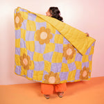 Girl standing holding the cool funky daisy pattern puffy blanket on an orange floor and pink background.