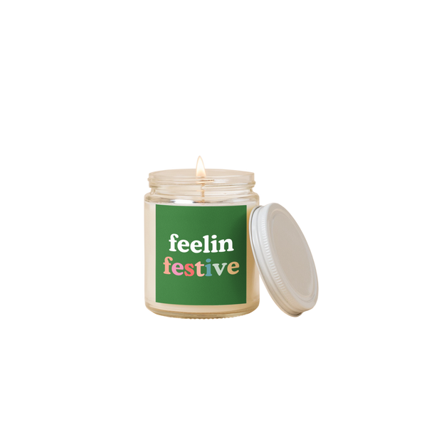 8 oz candle jar with green label on front with text that reads "feelin festive" in white and multi-color letters.